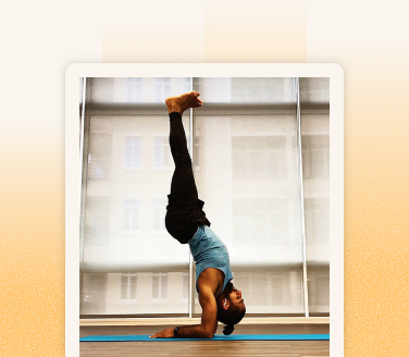 Gurveer Uppal performing a headstand on a blue yoga mat in a bright studio with large windows