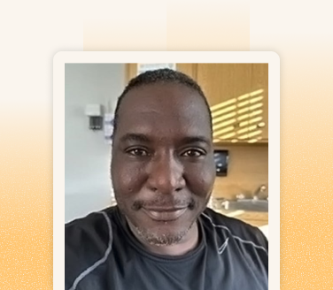 Darryl Blackman smiling in a selfie, wearing a dark athletic shirt, with wood cabinets and a sink visible behind him
