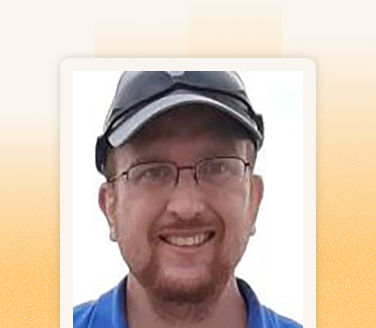 Brian smiling in a close-up portrait, wearing glasses and a dark baseball cap with a blue polo shirt