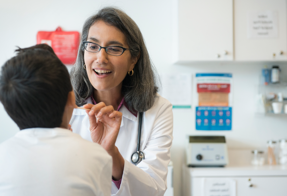 A smiling provider in a white coat talks with a child in an exam room