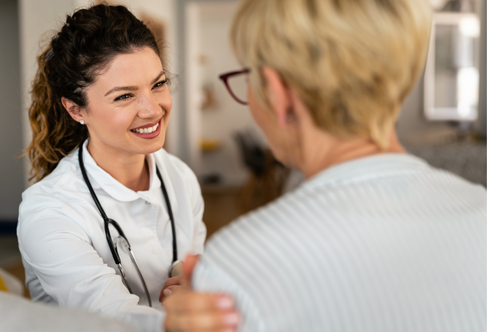 A smiling provider in a white coat rests a hand on the shoulder of a person during a visit