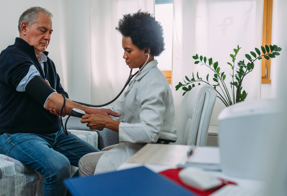 A provider in a white coat measures the blood pressure of a seated person at home