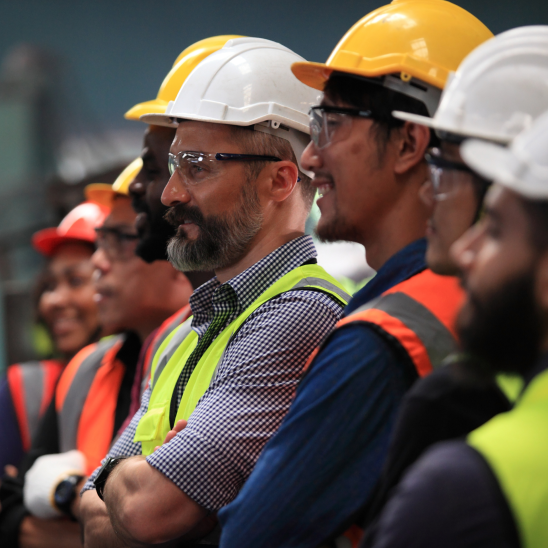 A row of workers in hard hats, safety glasses, and high-visibility vests standing together