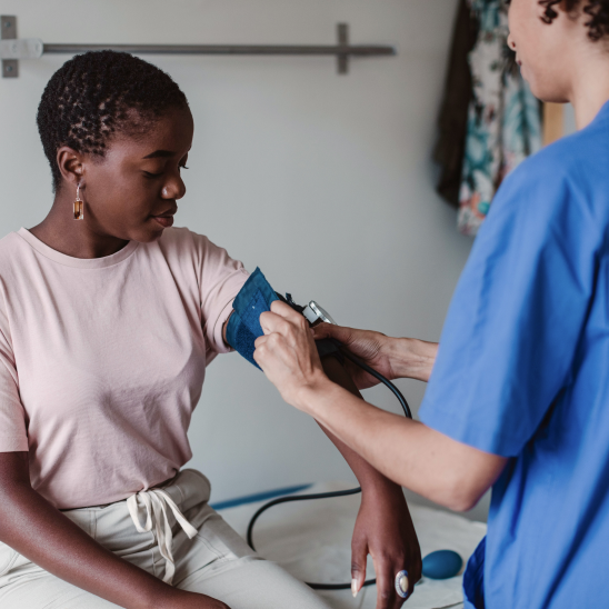 A provider in blue scrubs measures the blood pressure of a seated person