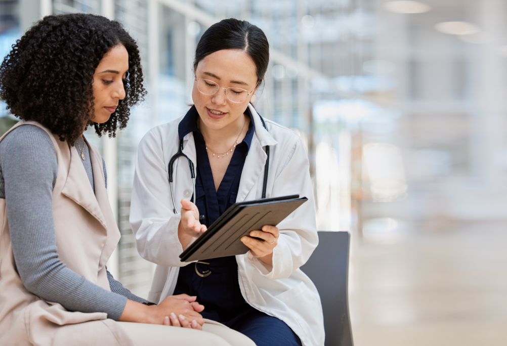 A provider in a white coat shows a tablet to a seated person during a consultation