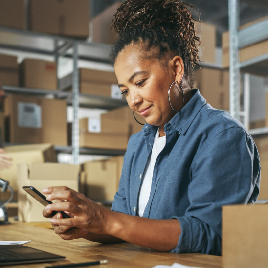 A person using a phone at a desk in a warehouse stocked with boxes